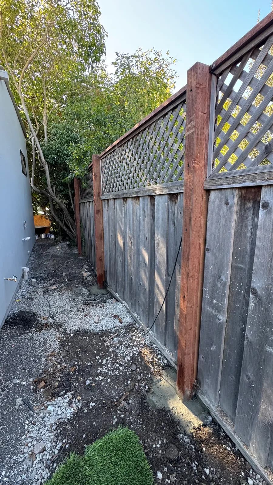 Grey weathered fence boards and lattice carried by two new redwood posts, fresh concrete at the near post base