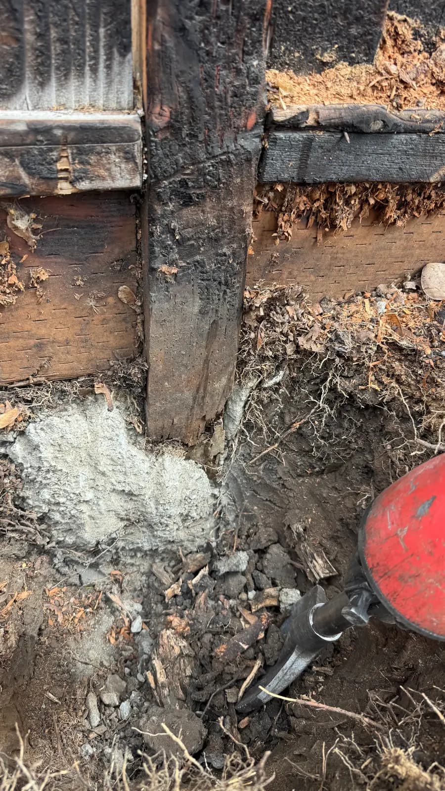 Excavated fence post base with the old concrete footing broken open, charred post and a digging bar beside it