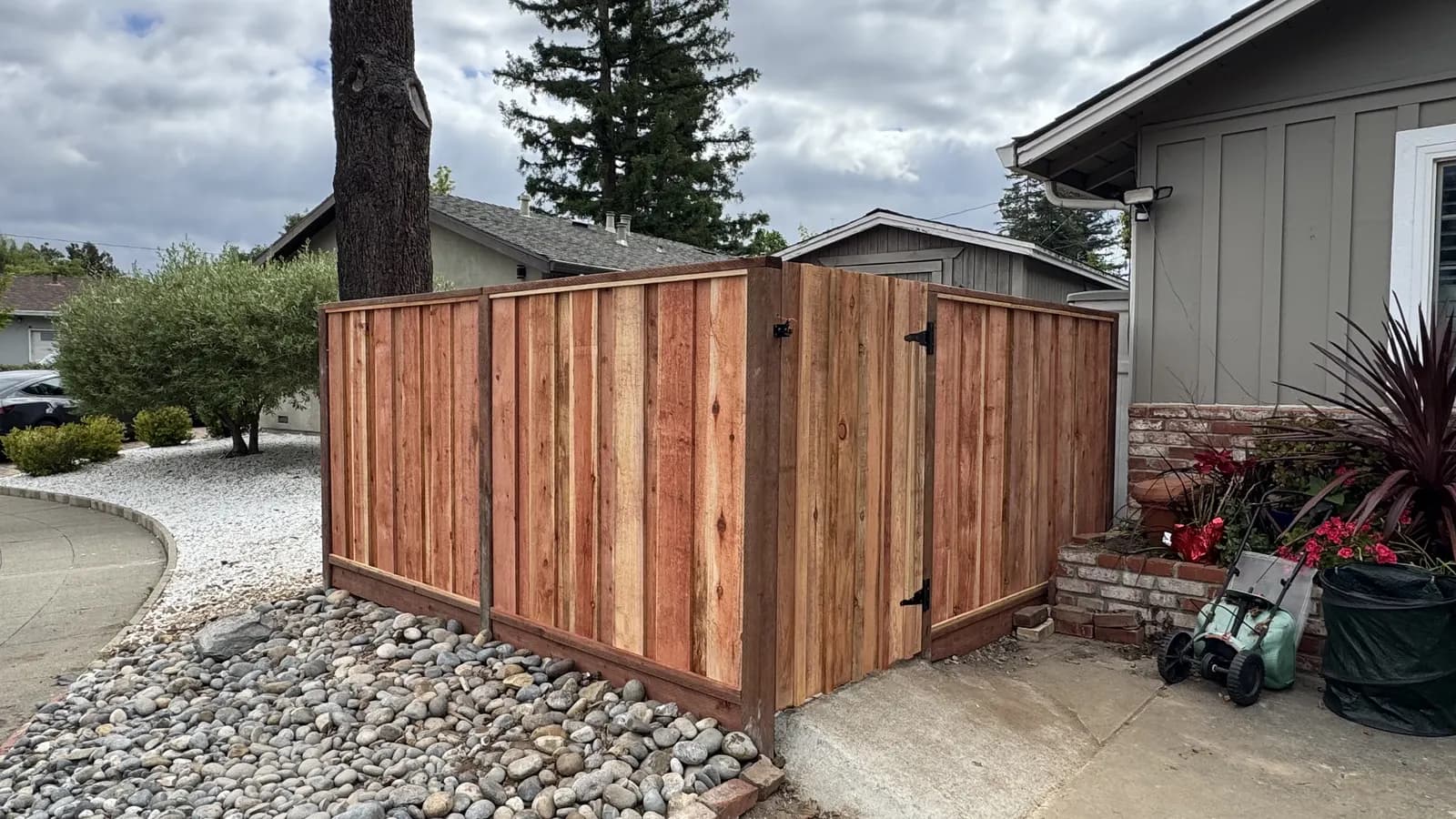 Redwood board fence and matching gate on black strap hinges, front garden with river rock and a driveway